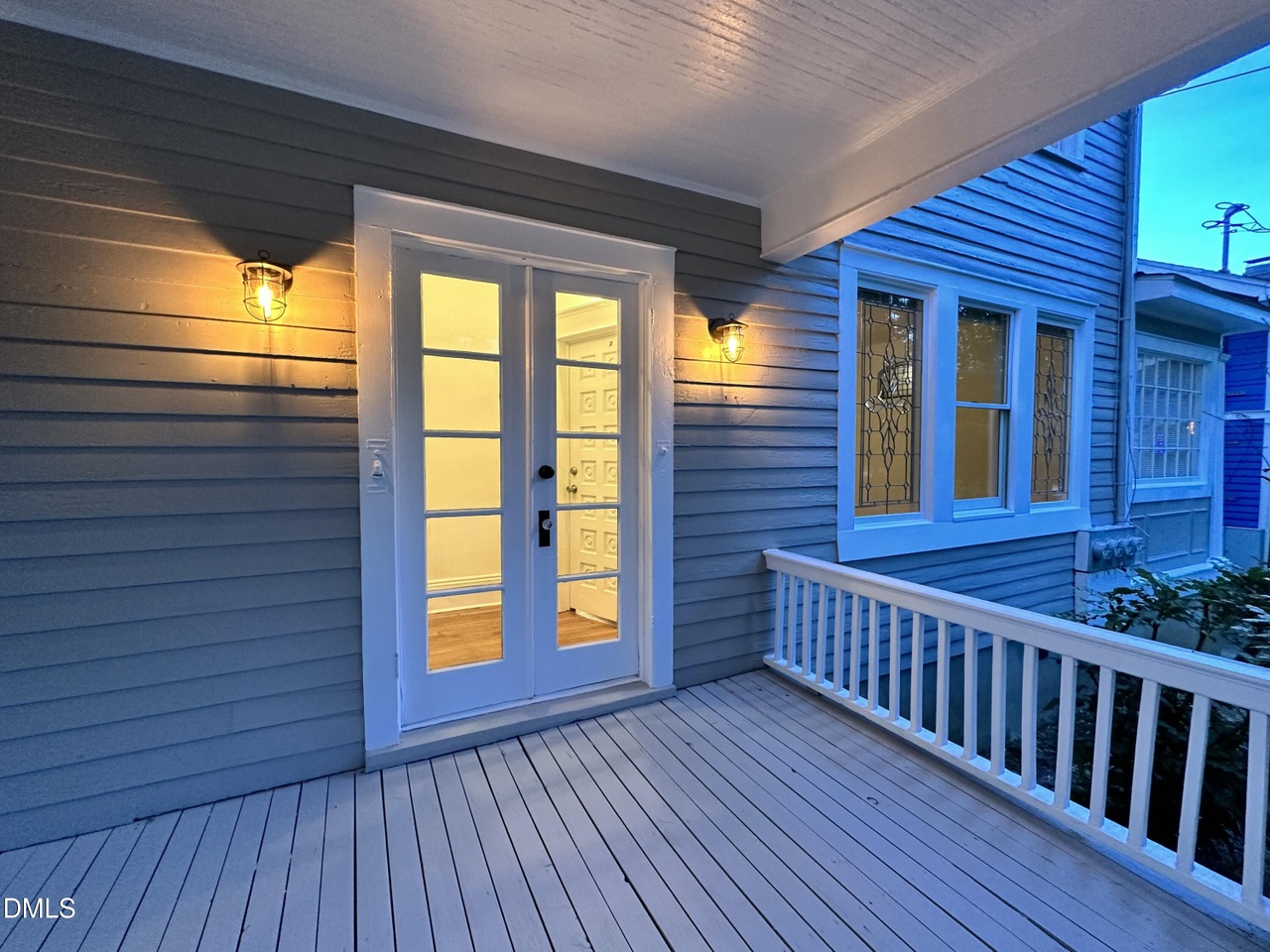 Covered porch at dusk with glowing lantern sconces, glass-paned French doors, and leaded-glass windows