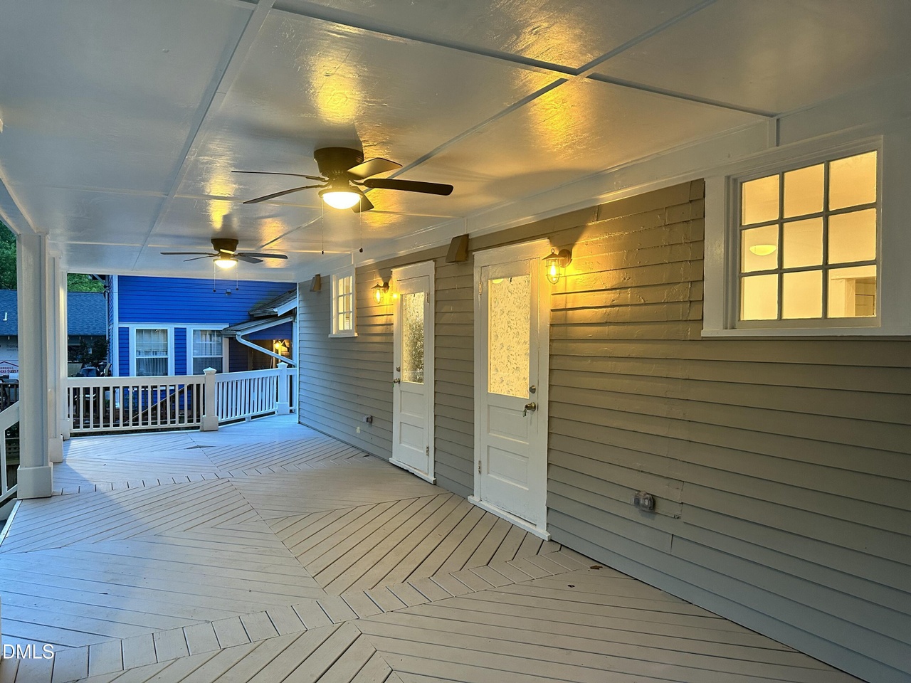 Wide covered lower porch with two ceiling fans, chevron-laid decking, lantern sconces, and two apartment doors