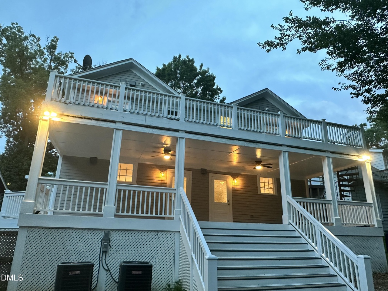Rear elevation of 1110 Glenwood Ave at dusk with two levels of white-railed porches, twin exterior staircases, and lit lanterns