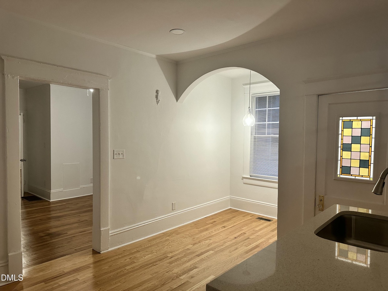 Arched dining alcove with a single pendant light, a window with blinds, and a stained-glass door beyond the kitchen counter