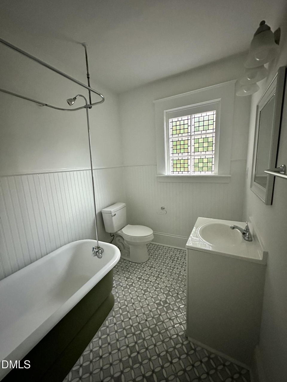 Bathroom with a green-skirted soaking tub, patterned tile floor, beadboard wainscot, and a stained-glass window