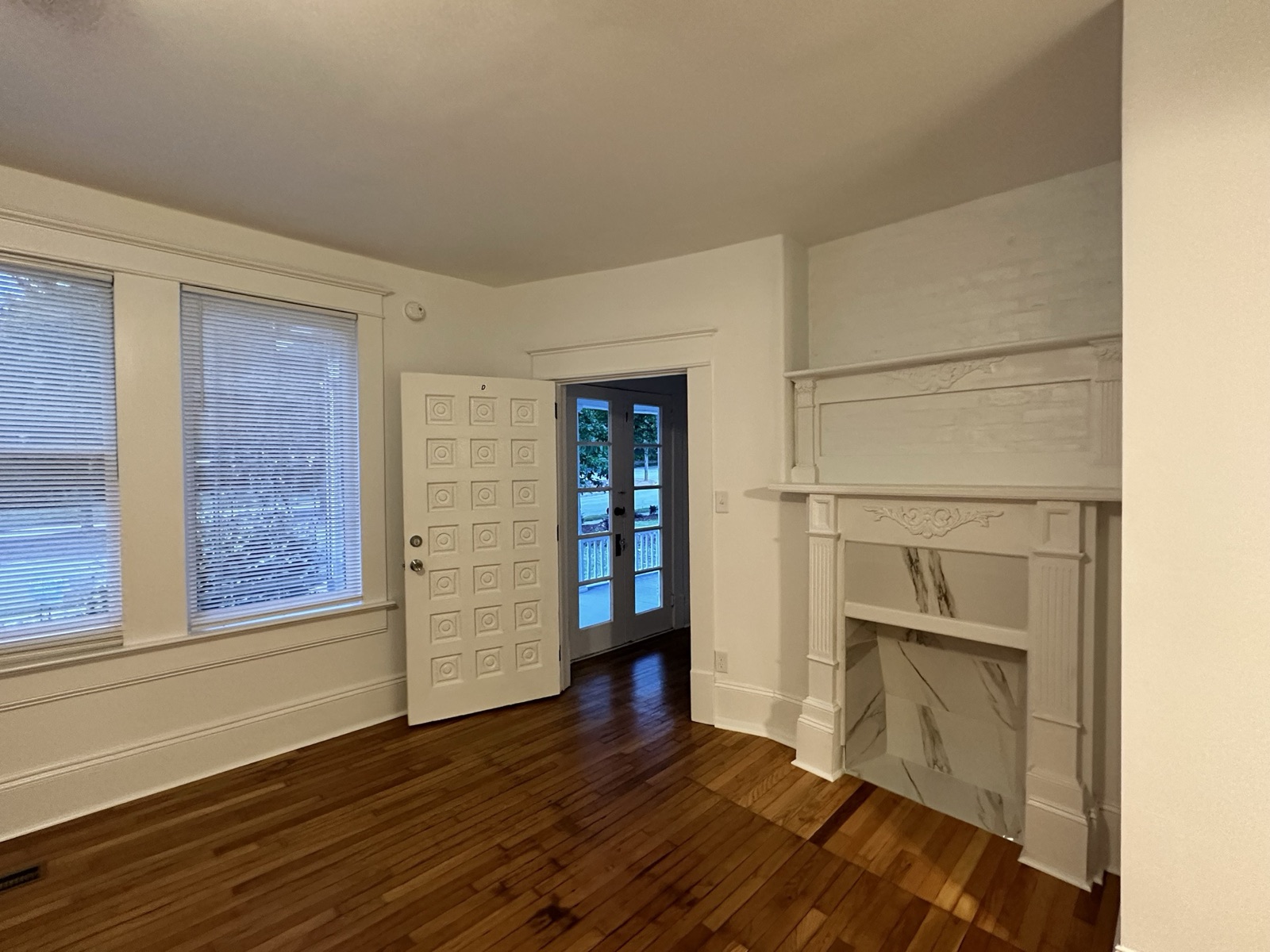 Living room at 1110 Glenwood Ave with an original white fireplace mantel and marble surround, hardwood floors, and a paneled door
