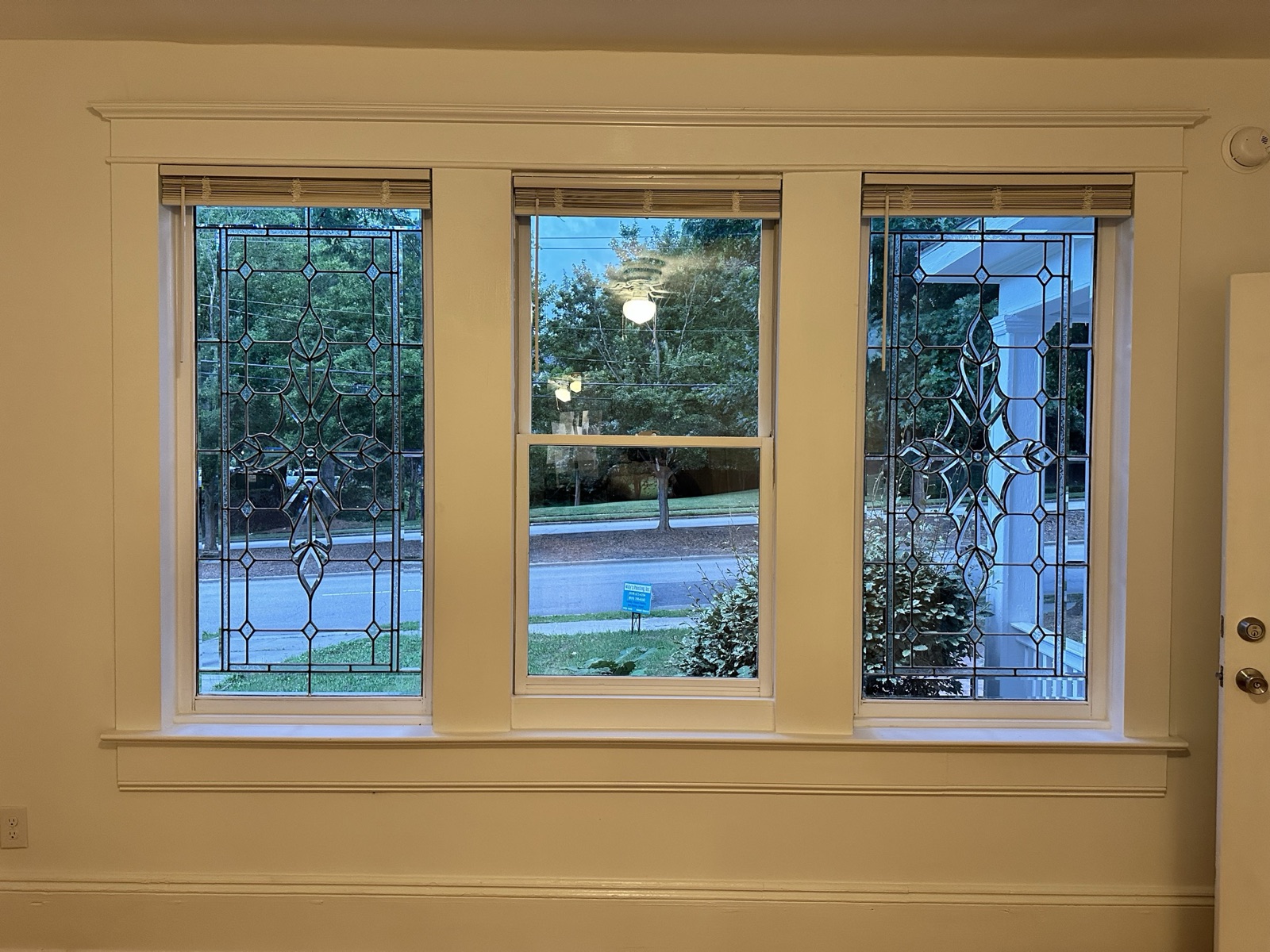 Triple window with leaded and beveled glass medallions in the flanking panes, looking out to the street and trees